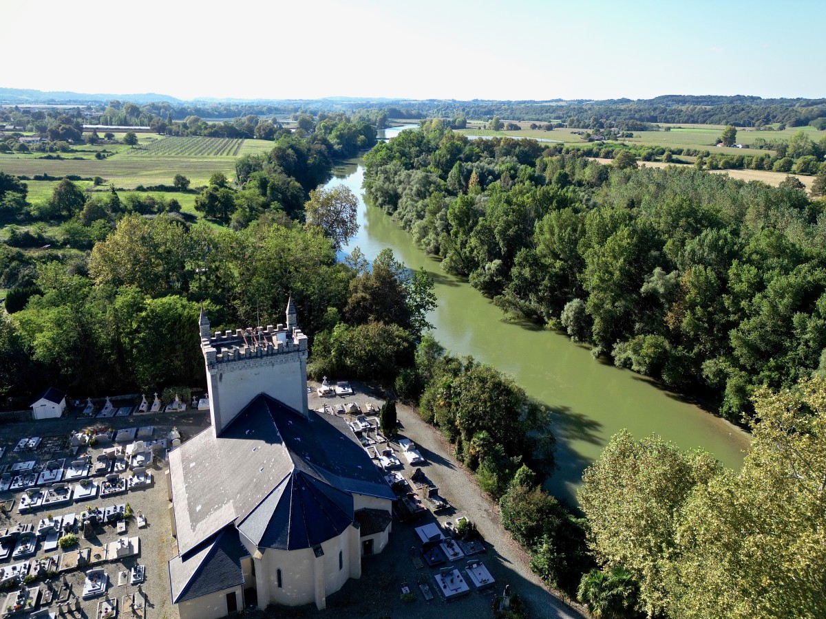 Photo prise par un drone au dessus du sanctuaire. À gauche le clocher crénelé qui ressemble à un donjon. À droite le gave de Pau. Beaucoup de végétation autour.